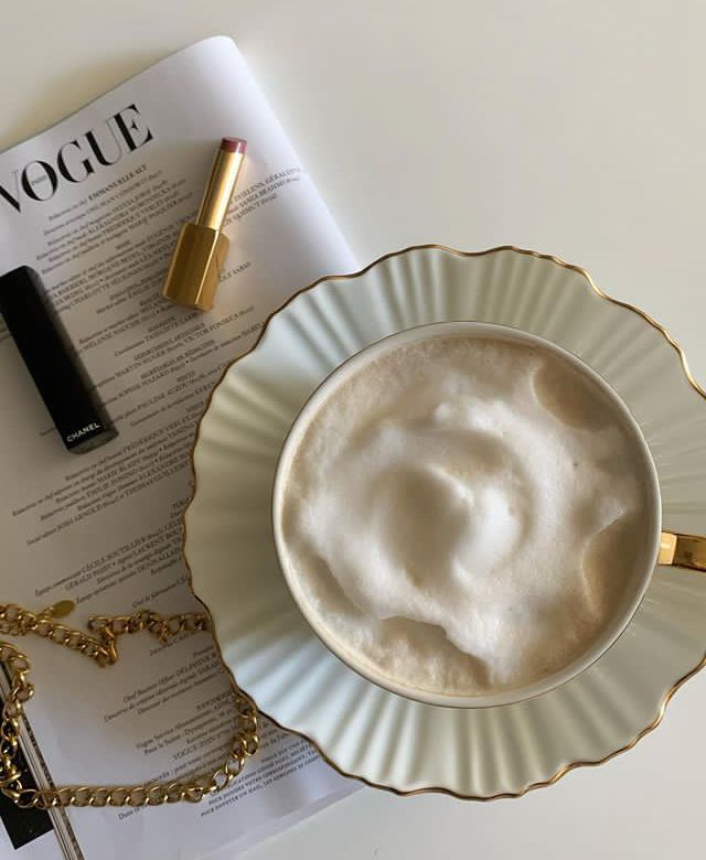 a cup of whipped cream next to a gold necklace and lipstick on top of a magazine