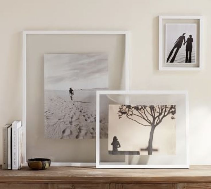 three framed photographs on a wooden table next to a book shelf with books and other items