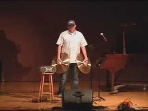 a man holding two drums while standing in front of a piano and microphone on stage