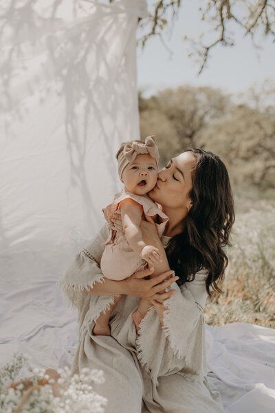 a woman holding a baby in her arms while she is kissing the baby's cheek