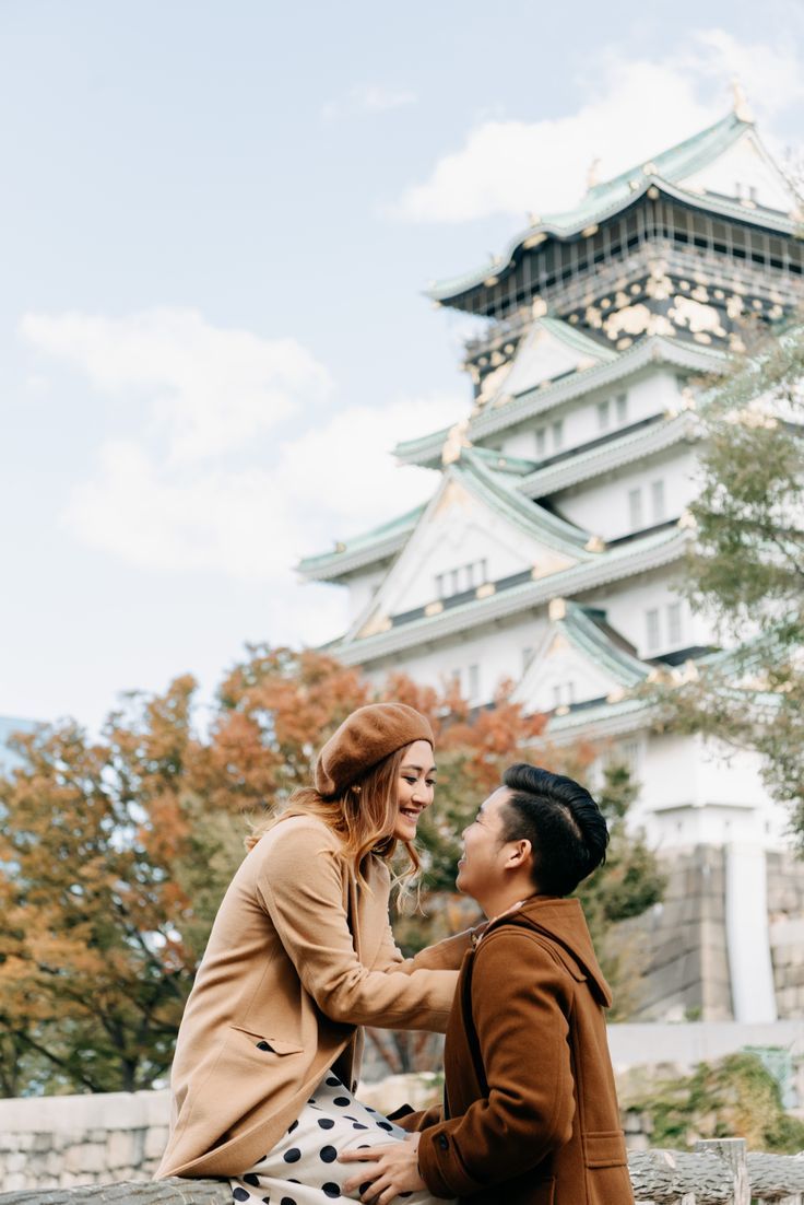 a man and woman sitting on the ground in front of a building with a tower