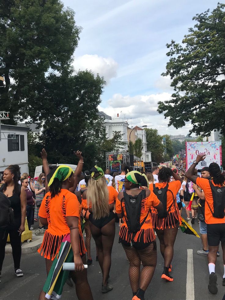 some people are walking down the street with orange shirts and green hats on their heads