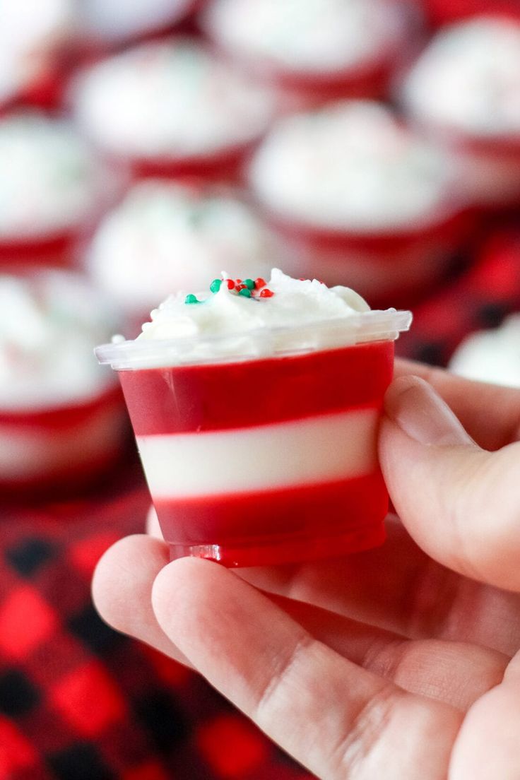 a hand holding a cupcake with white frosting and sprinkles on top