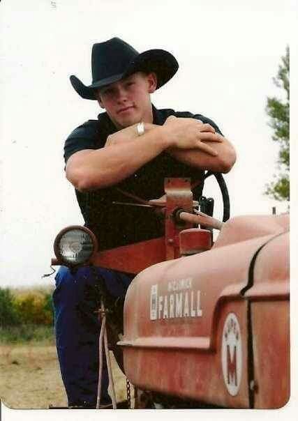 a man wearing a cowboy hat leaning on an old red farmall tractor with his arms crossed