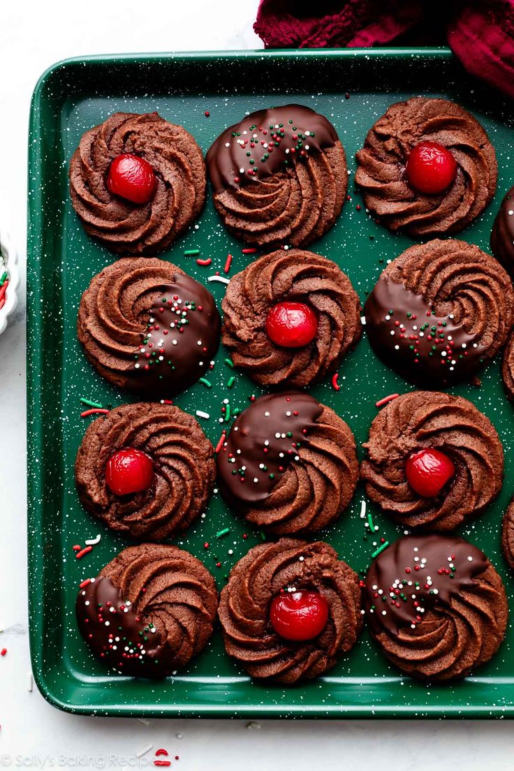 a green tray filled with chocolate covered cookies and cherries on top of a table