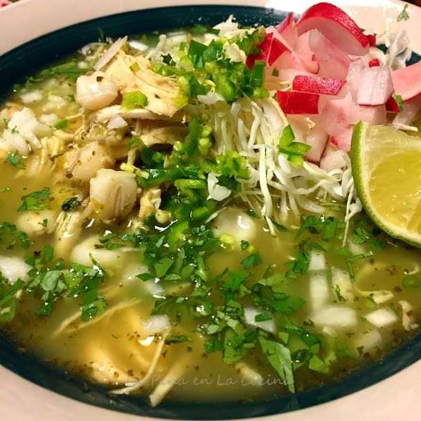 a white bowl filled with soup and garnished with cilantro, limes, red onion, and parsley