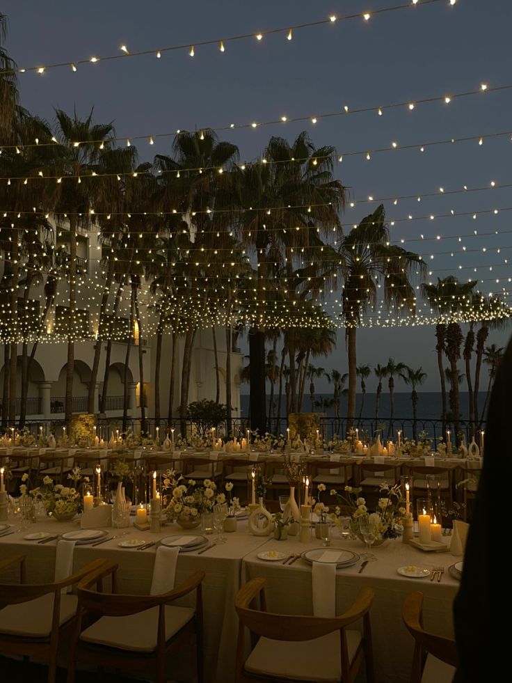 a long table is set up with candles and place settings in front of palm trees