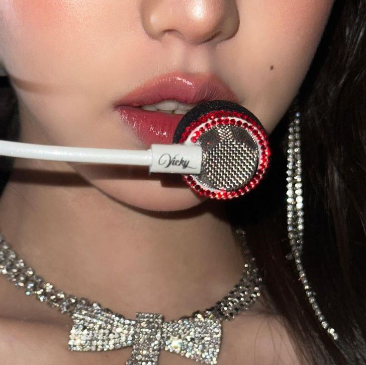 a close up of a person wearing a necklace and holding a microphone to her mouth