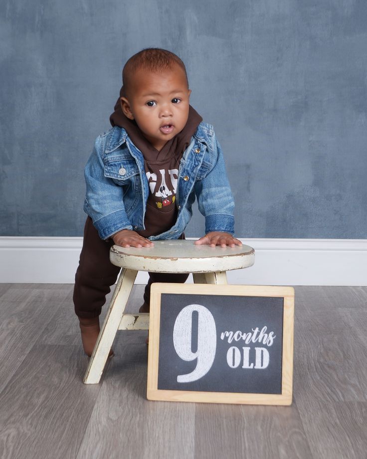 a baby sitting on a stool with a sign in front of him that says 9 months old