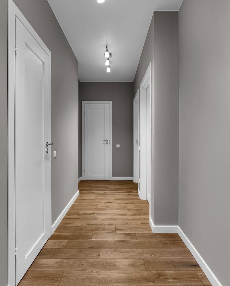 an empty hallway with light wood floors and white doors on either side of the room