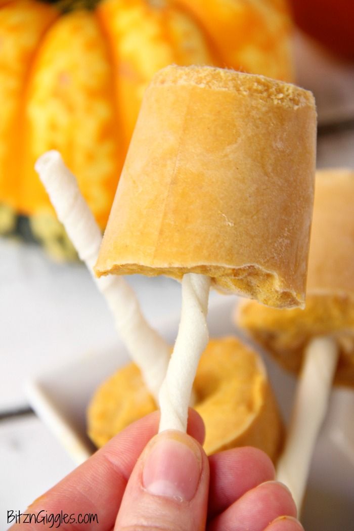 a hand holding an orange and white lollipop in front of some pumpkins