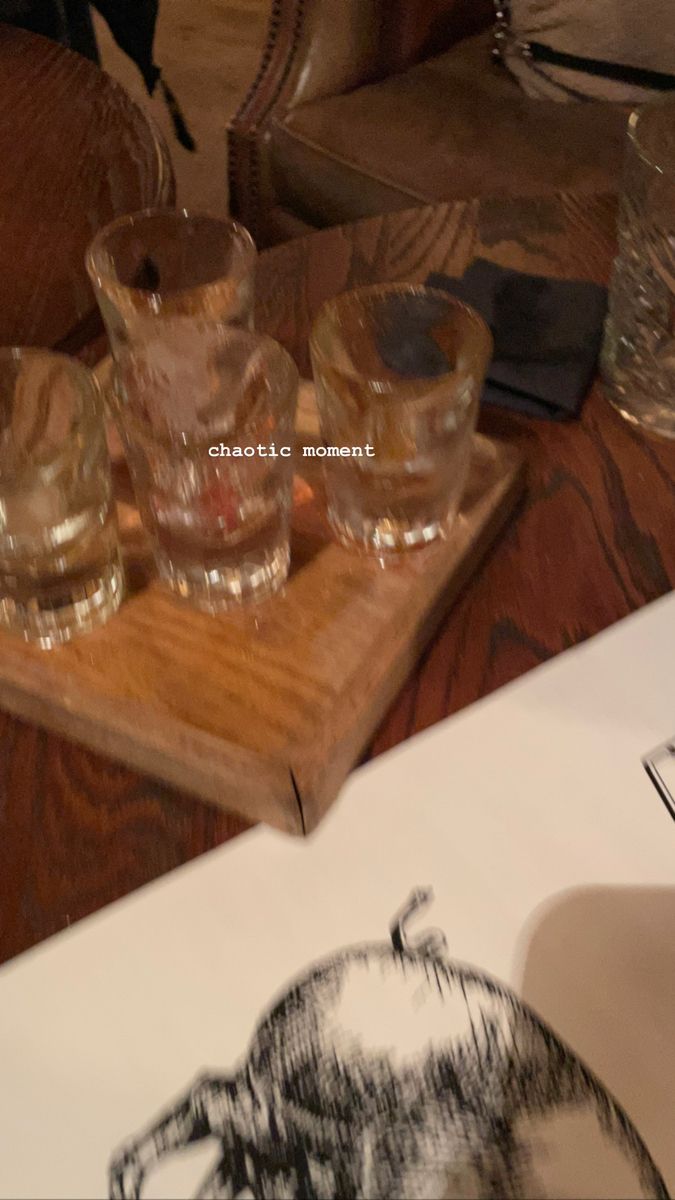 glasses are sitting on a wooden tray next to an open book and glassware in front of them