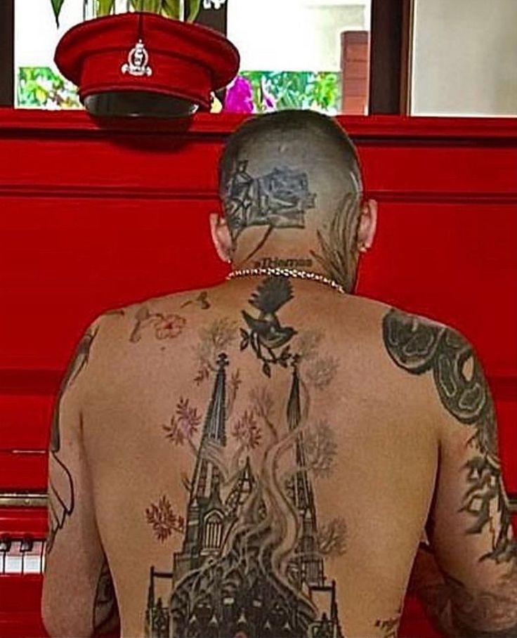 a man with tattoos on his back sitting in front of a red piano and looking at something