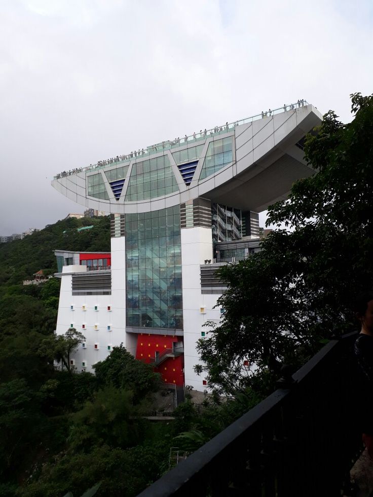 a large white building sitting on the side of a lush green hillside next to trees