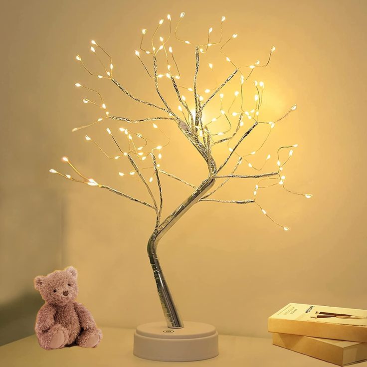 a teddy bear sitting next to a tree with lights on it's branches and a box