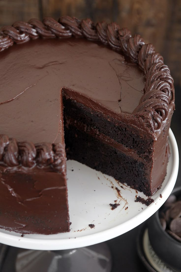 a chocolate cake on a white plate with one slice cut out and ready to be eaten