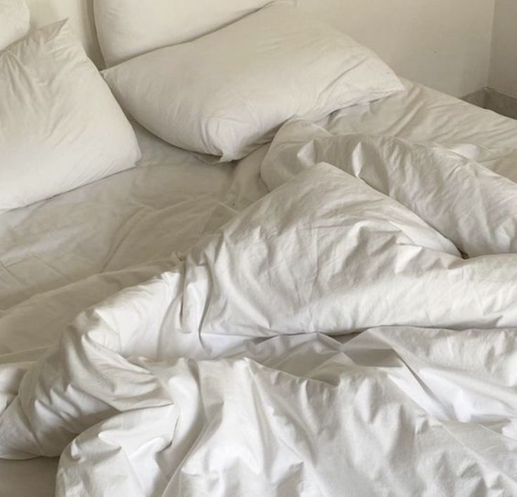 an unmade bed with white sheets and pillows