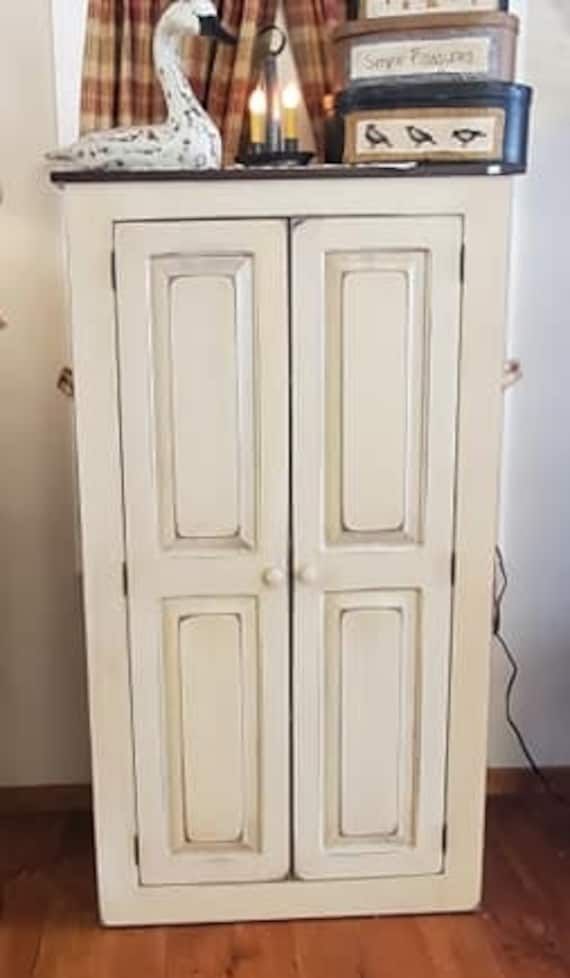 a tall white cabinet with two doors and a clock on it's top shelf