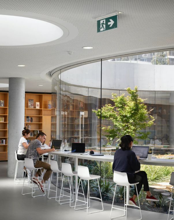 two people sitting at a long table with laptops in front of them and bookshelves behind them