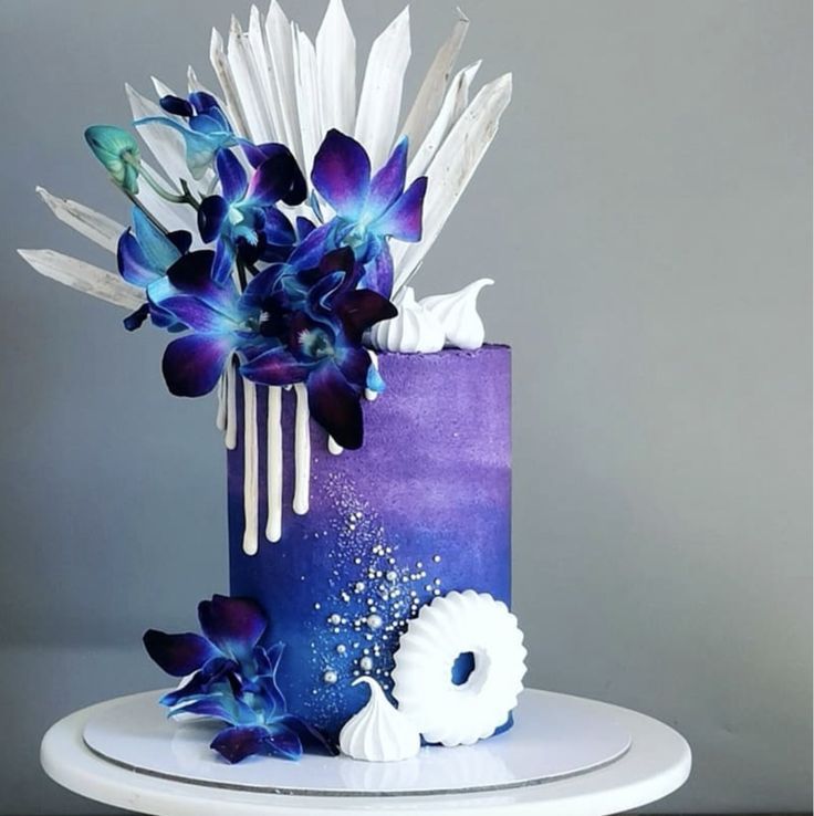 a blue and purple cake with white flowers on the top is sitting on a table