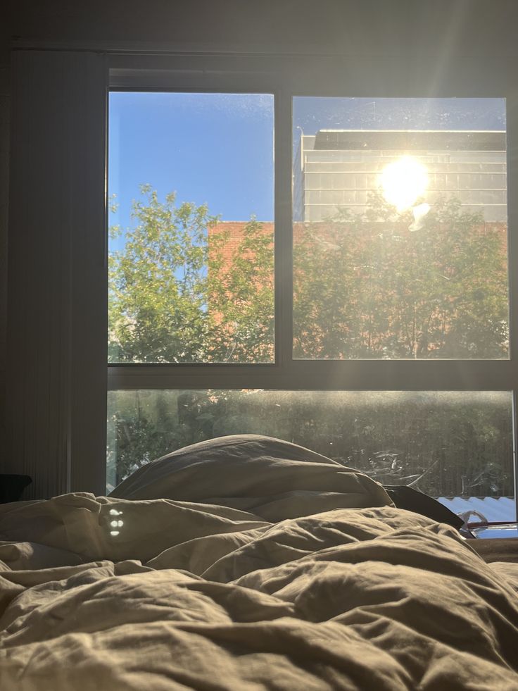 the sun shines brightly through two windows in a room with an unmade bed