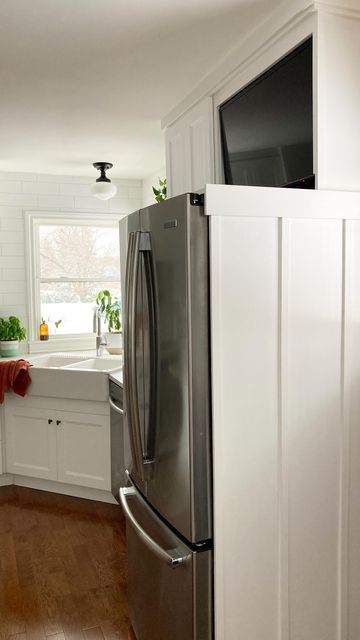 a stainless steel refrigerator in a kitchen with white cabinets and wood flooring on the side