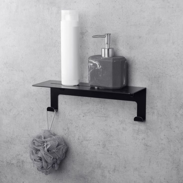 a black and white photo of a soap dispenser on a shelf next to a toilet paper roll