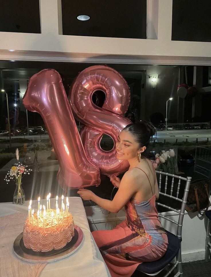 a woman sitting at a table with a birthday cake and large number balloon in front of her