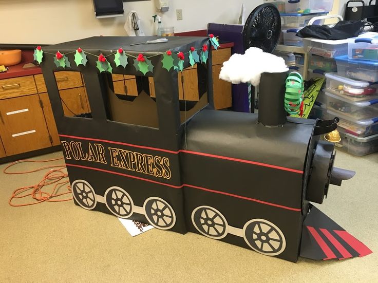 a cardboard train sitting on top of a floor next to a table with chairs and desks