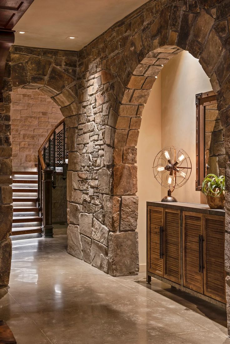 an arched doorway leads to a foyer with stone walls and flooring, along with a wooden cabinet