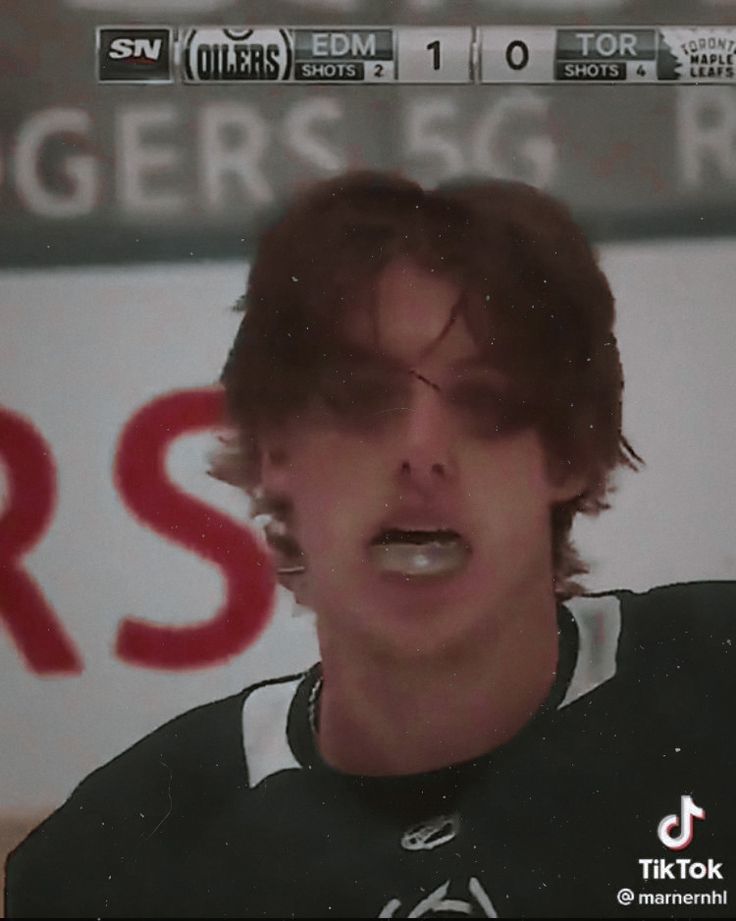 a young man with glasses on his face is standing in front of a hockey sign