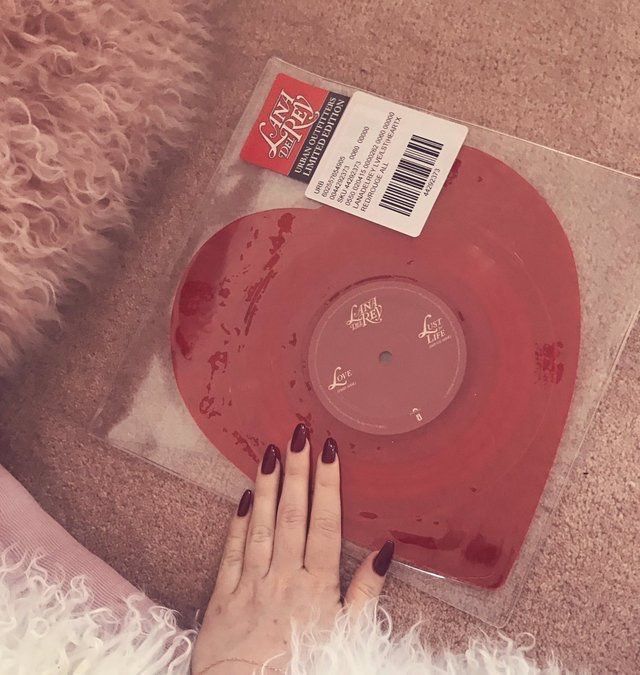 a woman's hand on top of a red record that is sitting on the floor