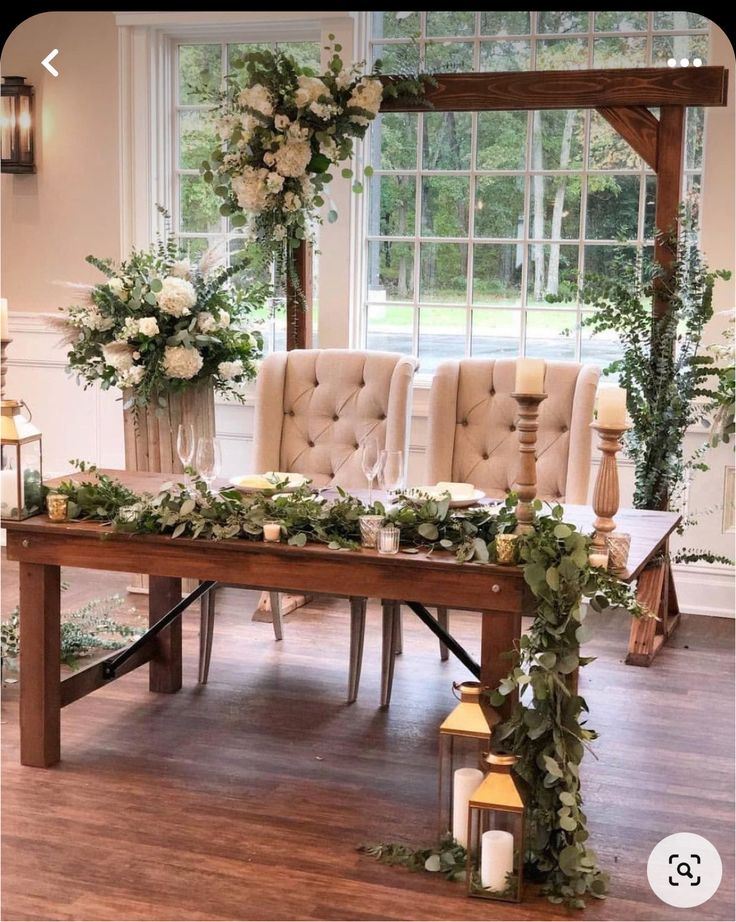 a table with candles, flowers and greenery on it in front of a window