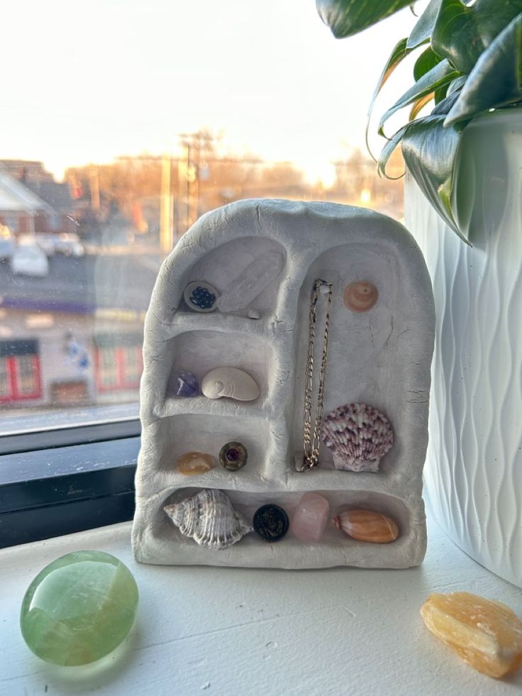 a white vase filled with lots of different types of items next to a window sill