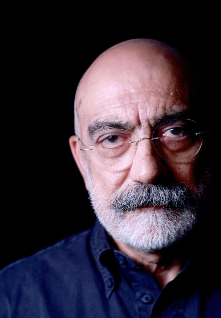 an older man with glasses and a beard looks at the camera while wearing a blue shirt