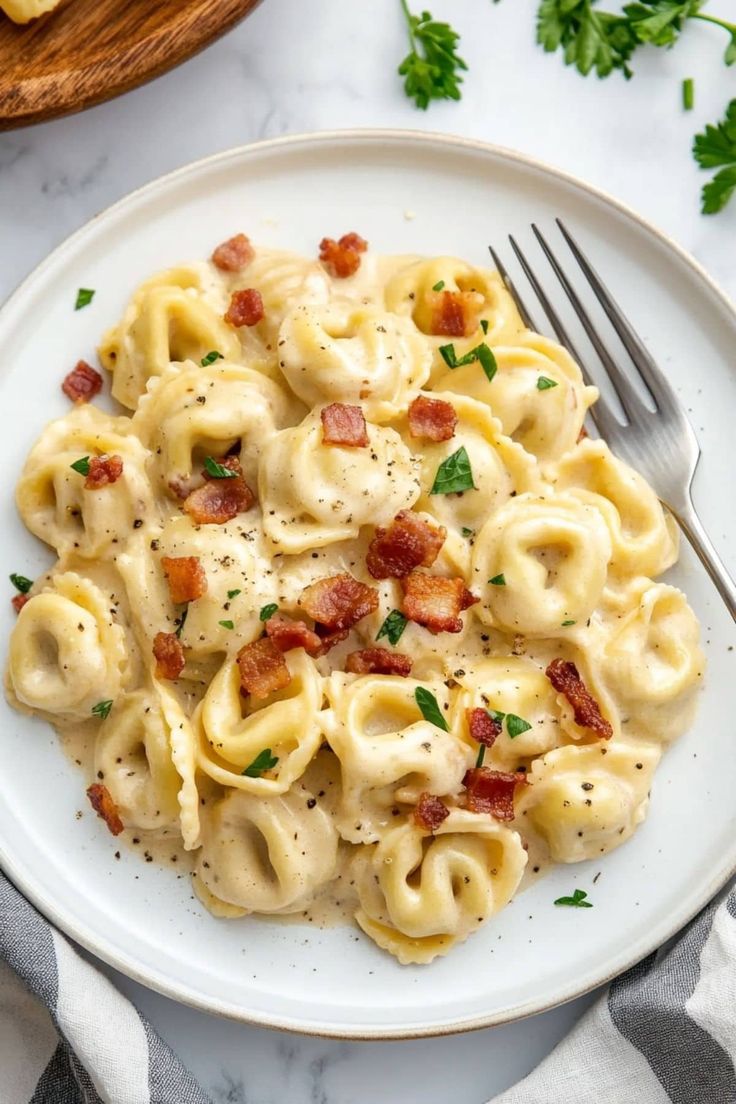 a white plate topped with tortellini shells covered in bacon and cheese, along with a fork