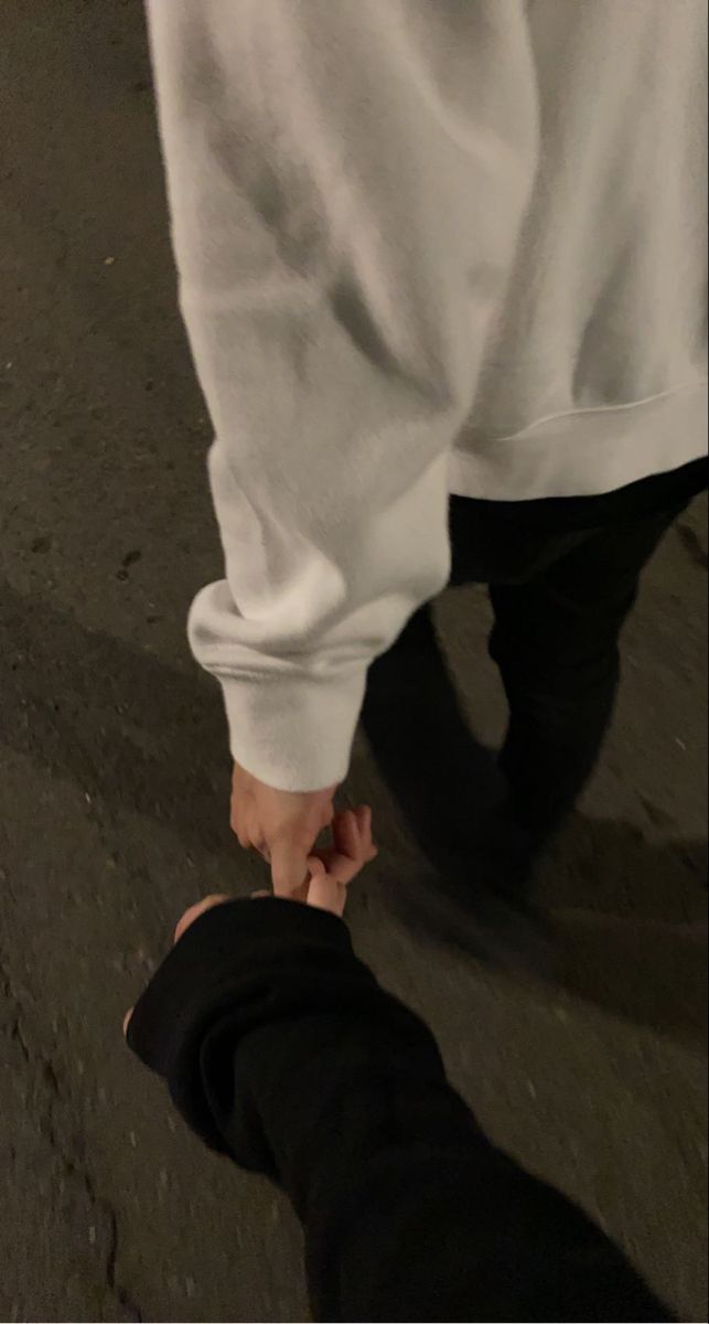 two people holding hands and walking down the street at night, one person has their hand in the other's pocket