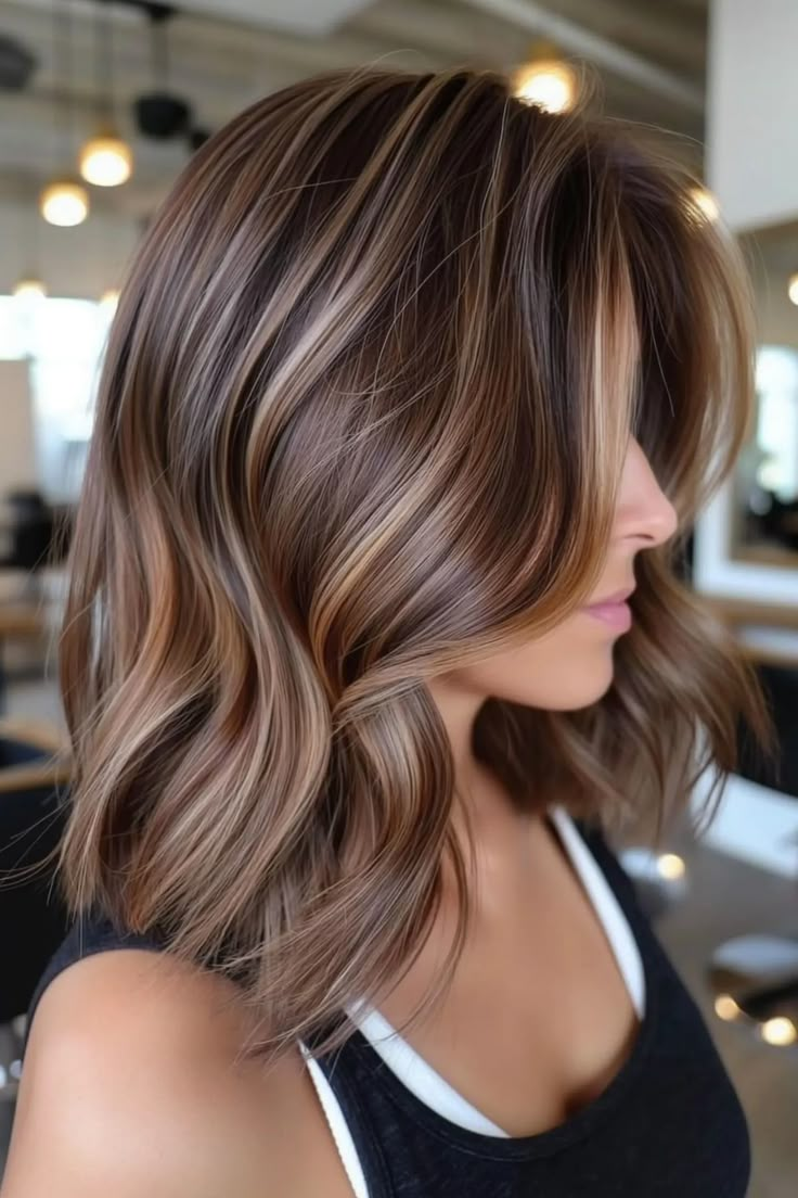 Woman with wavy, brown hair featuring blonde highlights in a salon. Hair Highlights On Dark Brown Hair, Short Caramel Hair With Highlights, Simple Highlights For Brown Hair, Short Medium Brown Hair With Highlights, Hazelnut Brown Hair Balayage, Short Hair Balayage Brunette Caramel, Caramel Highlights On Short Hair, Short Golden Brown Hair, Caramel Highlights Brown Hair Balayage