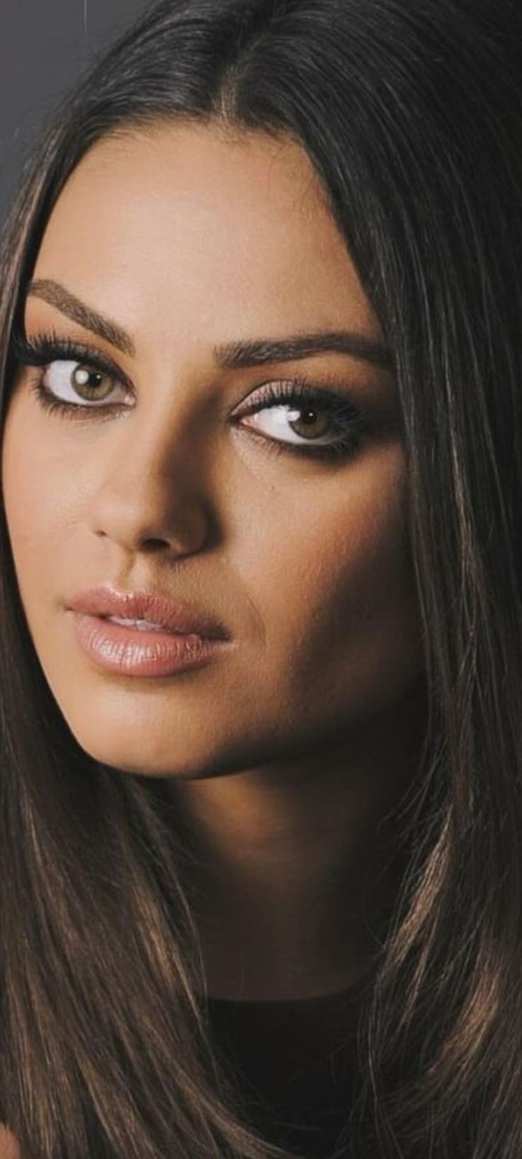 a woman with long brown hair and black eye makeup looks at the camera while posing for a photo