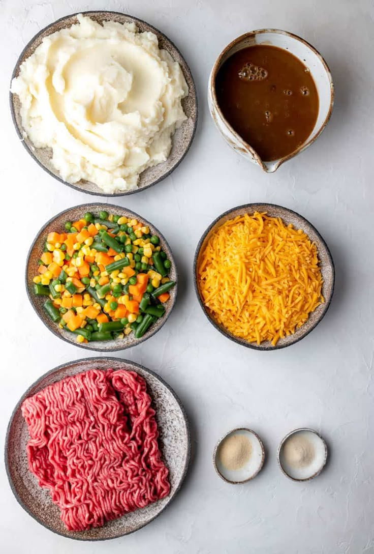 four different types of food in bowls on a white table with sauces and spoons