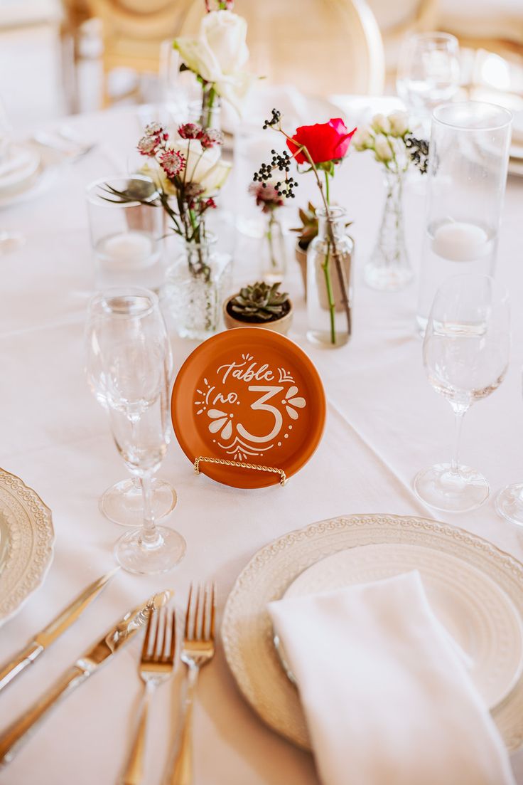 the table is set with plates, silverware and flowers