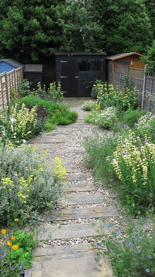 a garden with lots of flowers and plants growing on the side of it's path