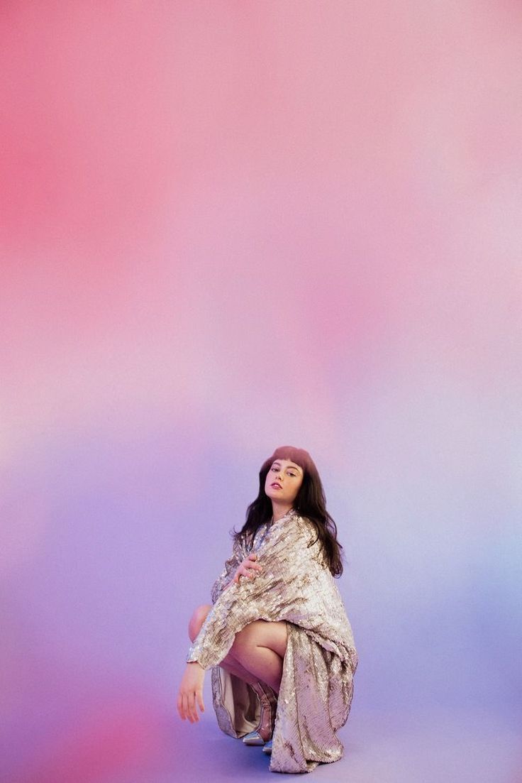 a woman sitting on the ground in front of a pink and blue background with her eyes closed