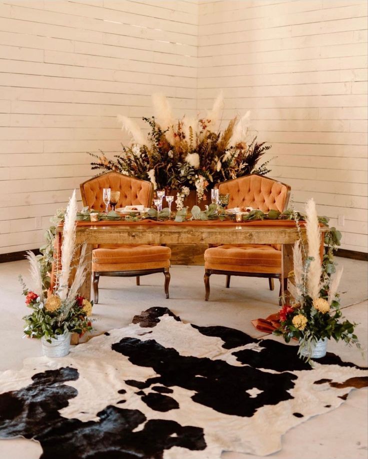 an arrangement of flowers and candles on a table with two chairs in front of it