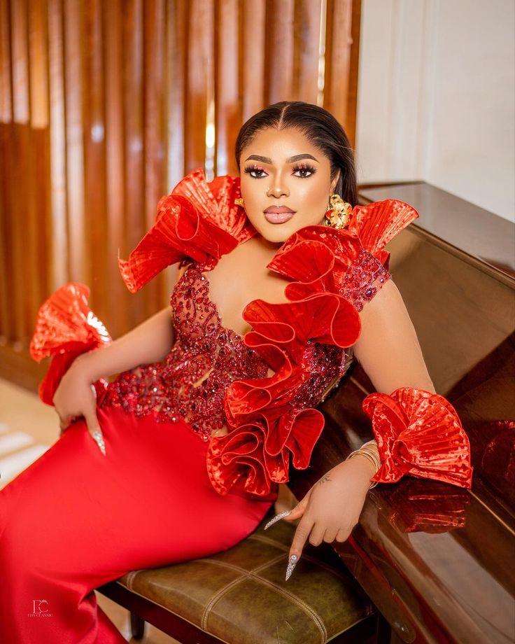 a woman in a red dress is sitting on a couch and posing for the camera