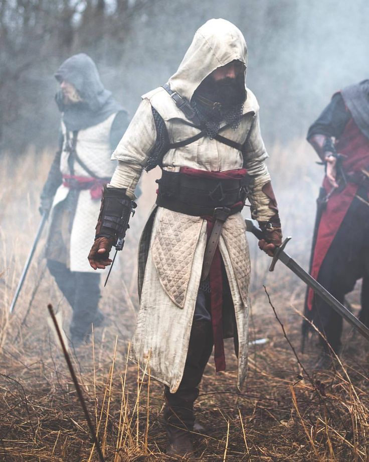 two men dressed in medieval clothing are walking through the woods with their swords and shields