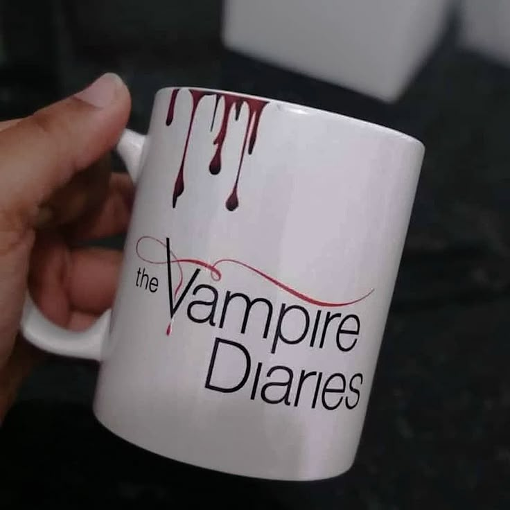 a person holding a coffee mug with the vampire's logo on it and dripping blood