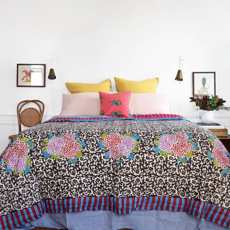 a bed with colorful pillows and blankets on top of it next to a wooden table