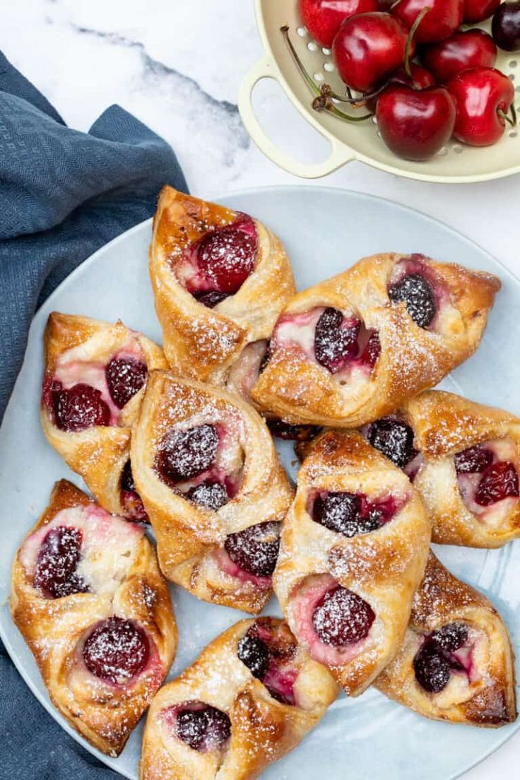 cherry pastries on a plate with powdered sugar and fresh cherries in the background