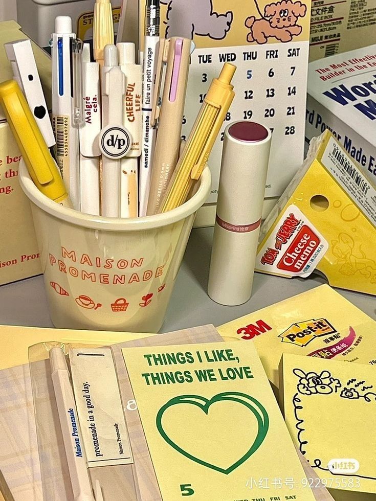 there are many pens and pencils in the cup on the desk next to books